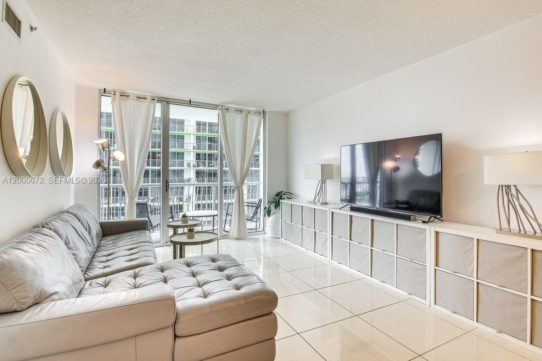 A modern living room features a tufted sectional sofa, white storage units, and a balcony — 1750 N Bayshore Dr # 1909, Miami FL 33132, MIAMI, FL