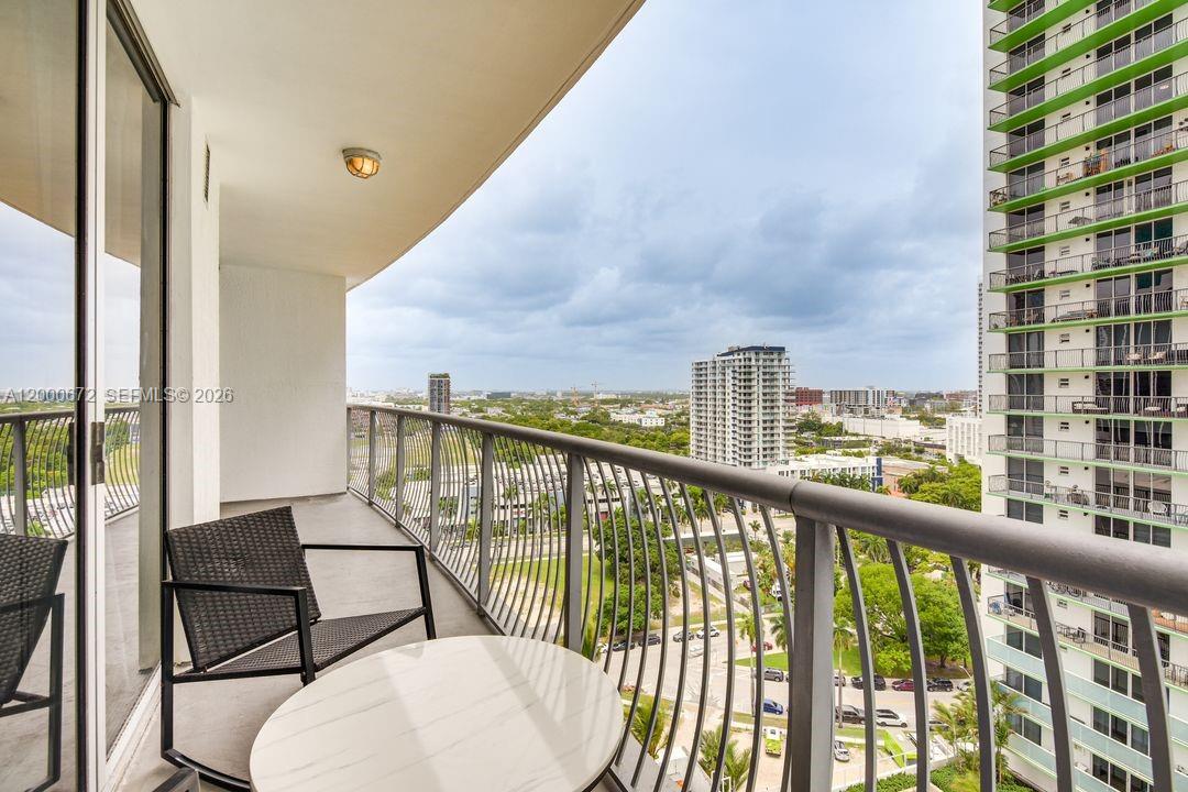 A balcony with a table and chairs overlooks a city landscape and a tall building — 1750 N Bayshore Dr # 1909, Miami FL 33132, MIAMI, FL