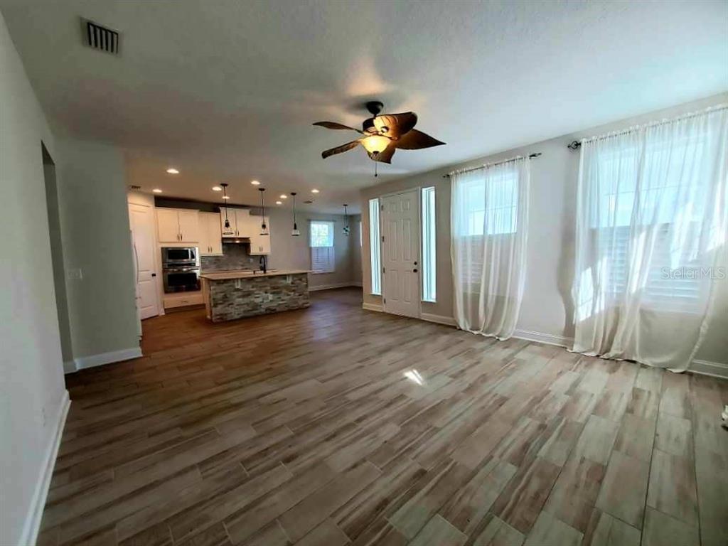 An open-concept living area features wood-look tile flooring, a ceiling fan, and a kitchen island — 37 SANDY BEACH WAY, PALM COAST, FL