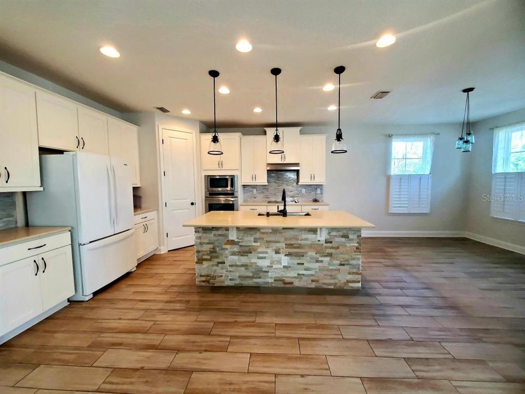 A kitchen features white cabinets, a stone-faced island, and wood-look tile flooring — 37 SANDY BEACH WAY, PALM COAST, FL