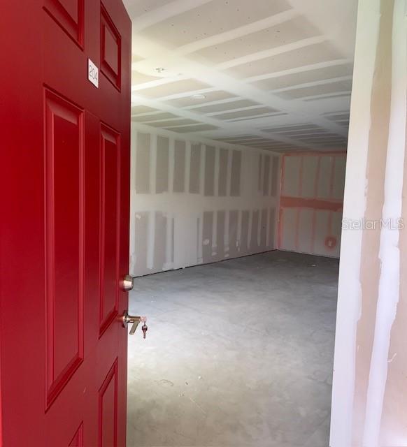An open red door reveals an unfinished room with bare drywall and concrete flooring — 3024 PARKWAY BOULEVARD UNIT 204, KISSIMMEE, FL