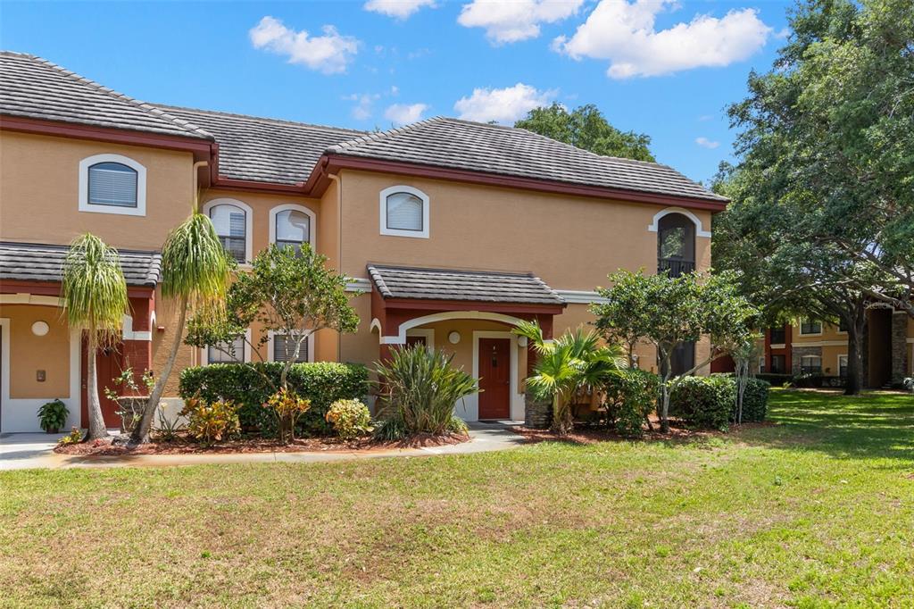 A screened-in patio features two black chairs overlooking a grassy courtyard and apartment buildings — 2200 TUSCANY TRACE UNIT 15, PALM HARBOR, FL