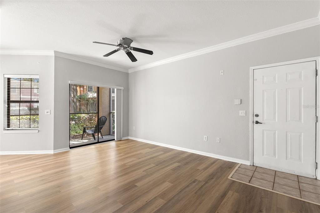 An empty living room with light gray walls, wood-look flooring, a ceiling fan, and sliding doors — 2200 TUSCANY TRACE UNIT 15, PALM HARBOR, FL