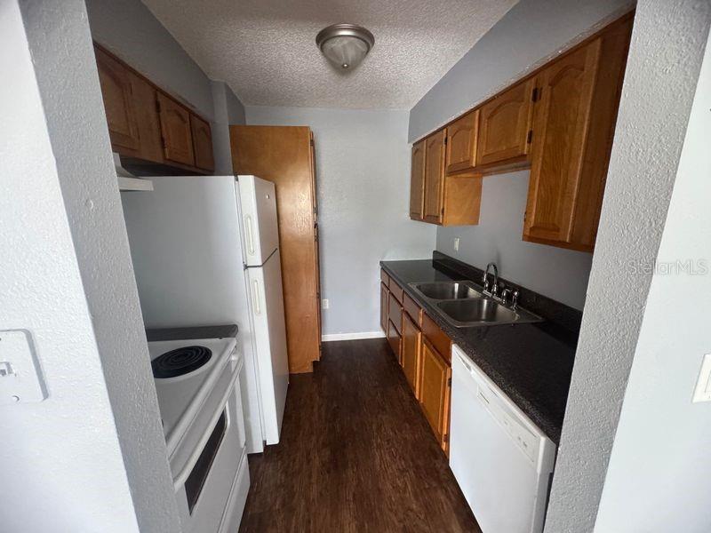 A galley kitchen features wood cabinets, dark countertops, white appliances, and wood-look flooring — 3544 PORTILLO ROAD UNIT 6, SPRING HILL, FL