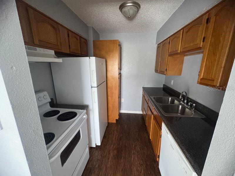A galley kitchen features wood cabinets, dark countertops, white appliances, and wood-look flooring — 3544 PORTILLO ROAD UNIT 6, SPRING HILL, FL