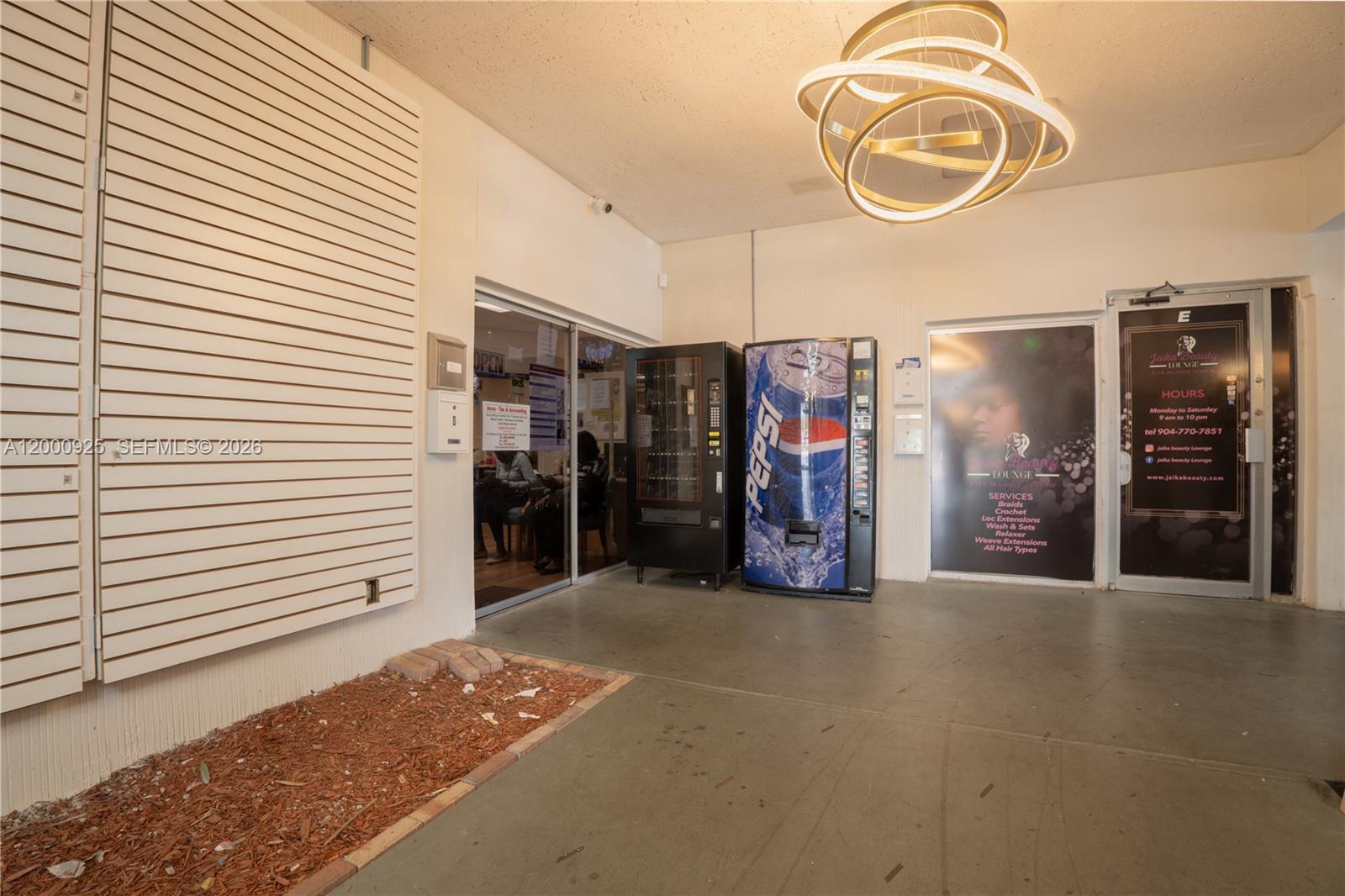A covered outdoor walkway features a Pepsi vending machine, a beauty salon entrance, and lighting — 6115 Miramar Pkwy, Miramar FL 33023, MIRAMAR, FL