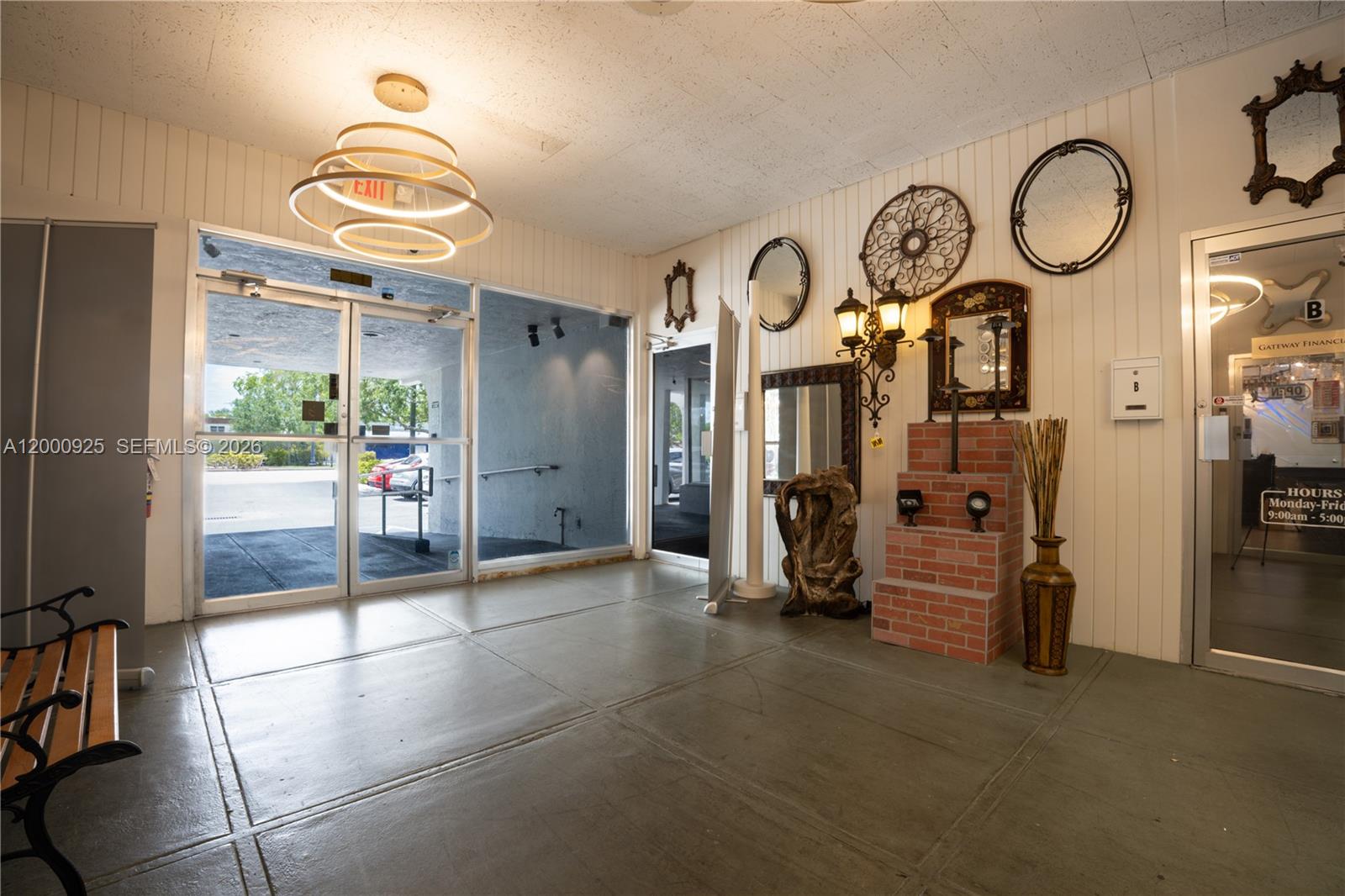 A commercial building lobby features a glass entrance, concrete floors, and decorative wall-mounted mirrors — 6115 Miramar Pkwy, Miramar FL 33023, MIRAMAR, FL