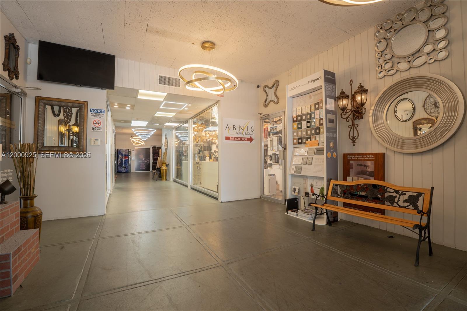 A commercial hallway features a bench, wall mirrors, lighting displays, and a glass-fronted storefront — 6115 Miramar Pkwy, Miramar FL 33023, MIRAMAR, FL