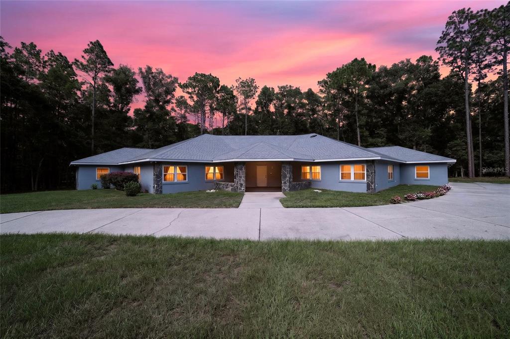 A wide, single-story gray house with stone accents sits behind a large concrete driveway — 7705 SW 186 AVENUE, DUNNELLON, FL
