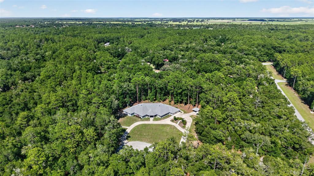 An aerial view shows a large house with a gray roof surrounded by dense forest — 7705 SW 186 AVENUE, DUNNELLON, FL