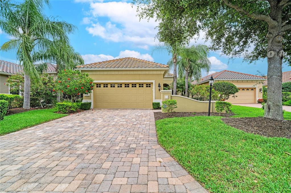 A tan house with a paver driveway, a two-car garage, and palm trees in front — 7361 WEXFORD COURT, LAKEWOOD RANCH, FL