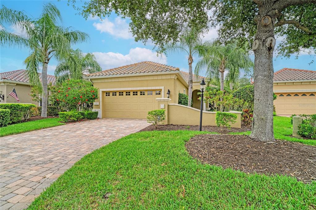 A tan stucco house with a tiled roof, a paved driveway, and palm trees — 7361 WEXFORD COURT, LAKEWOOD RANCH, FL