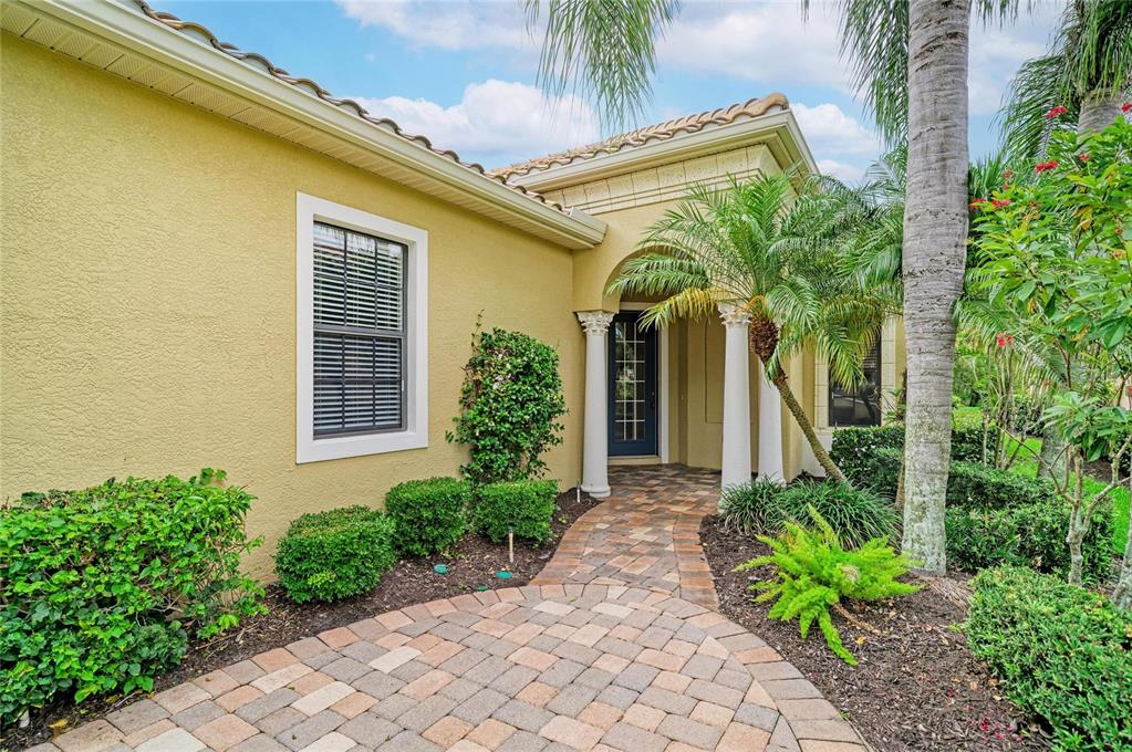 A paved walkway leads to the front entrance of a house with yellow stucco walls — 7361 WEXFORD COURT, LAKEWOOD RANCH, FL