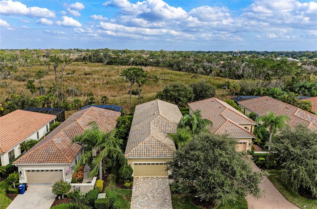 An aerial view shows three suburban houses with tiled roofs and driveways bordering a field — 7361 WEXFORD COURT, LAKEWOOD RANCH, FL
