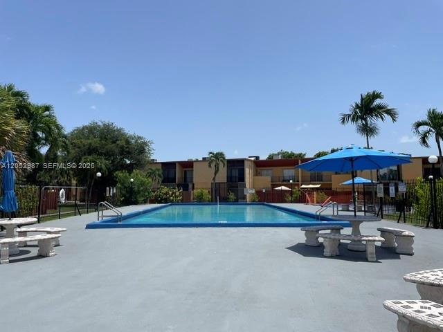 A rectangular swimming pool is surrounded by a concrete deck with outdoor tables and umbrellas — 13721 SW 84th St # G, Miami FL 33183, MIAMI, FL