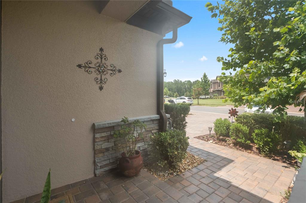 A paved entryway features a stone-accented wall, a decorative metal wall hanging, and potted plants — 4833 SAN MARTINO DRIVE, WESLEY CHAPEL, FL