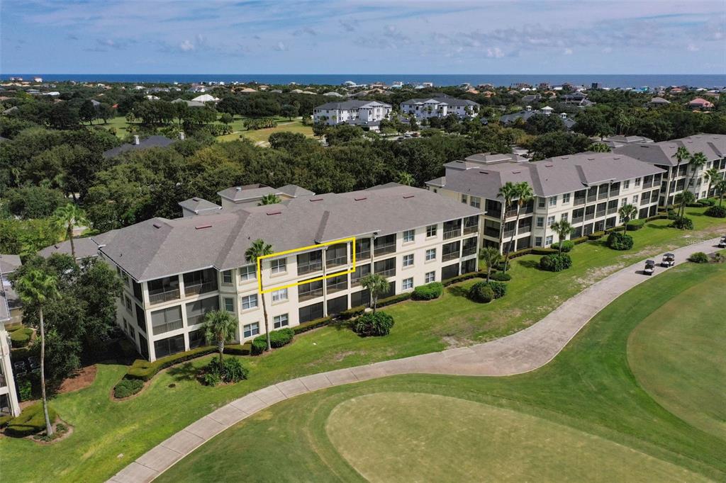 An aerial view of a multi-story apartment building overlooking a golf course and the ocean — 200 RIVERFRONT DRIVE UNIT B303, PALM COAST, FL