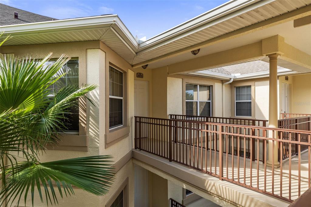 An exterior view of a second-floor apartment balcony with metal railings and a palm tree — 200 RIVERFRONT DRIVE UNIT B303, PALM COAST, FL