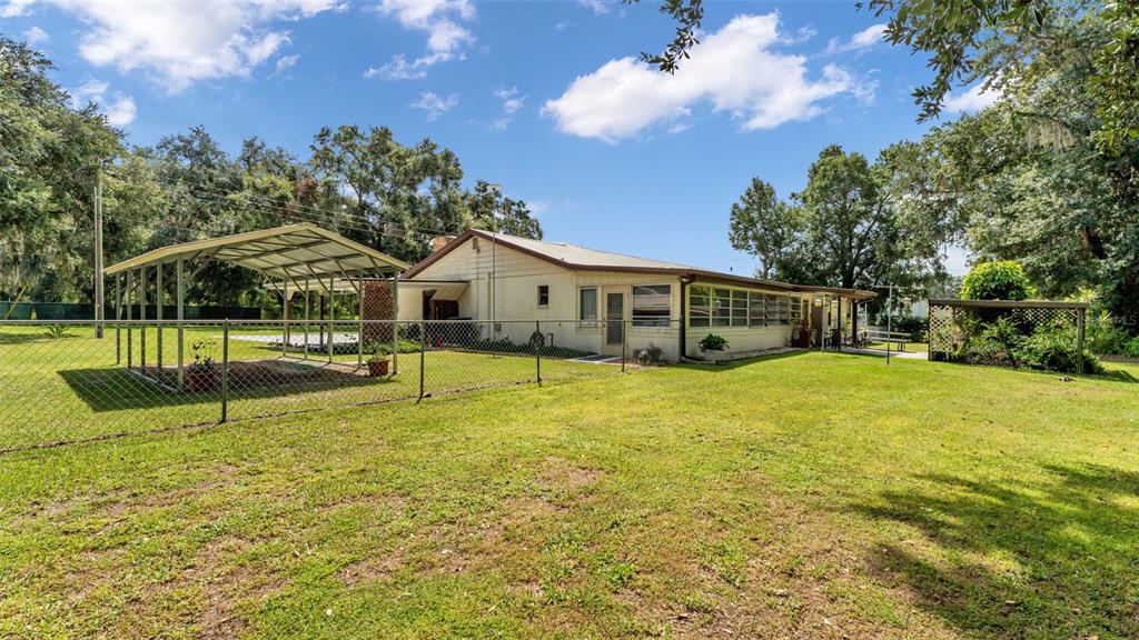 A single-story house with a metal carport stands in a large, grassy, fenced backyard — 1301 LANIER ROAD, LAKELAND, FL