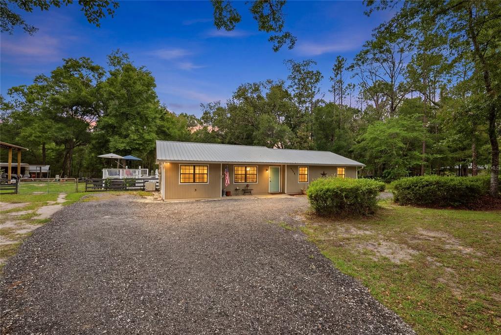 A single-story house with a metal roof and gravel driveway sits on a wooded lot — 10008 SW 80TH WAY, GAINESVILLE, FL