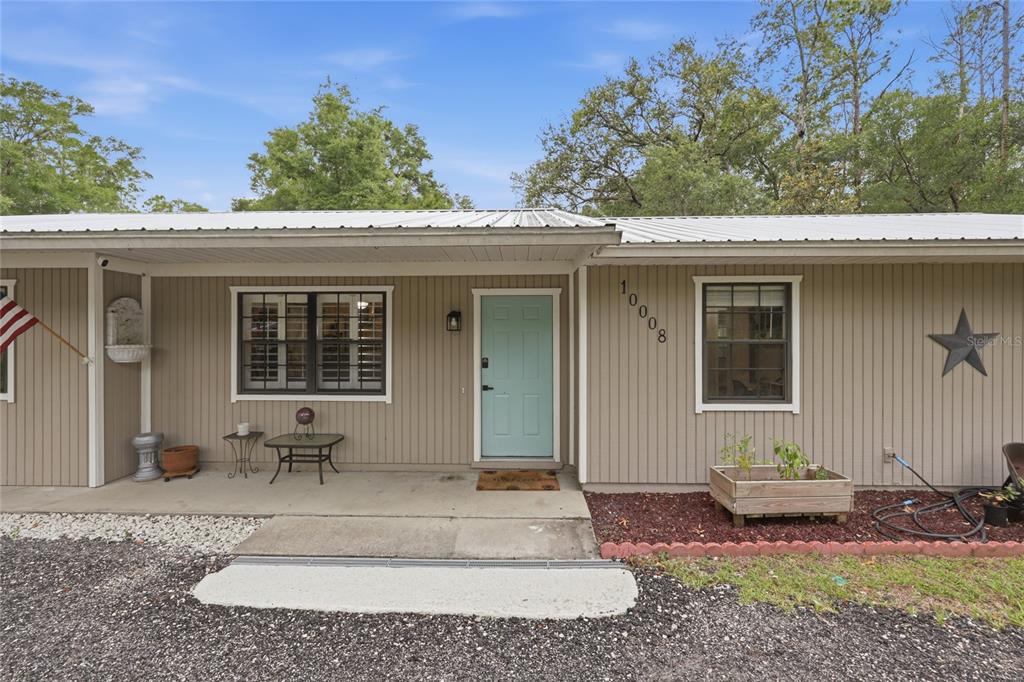 The exterior of a single-story house features light brown vertical siding and a light blue door — 10008 SW 80TH WAY, GAINESVILLE, FL