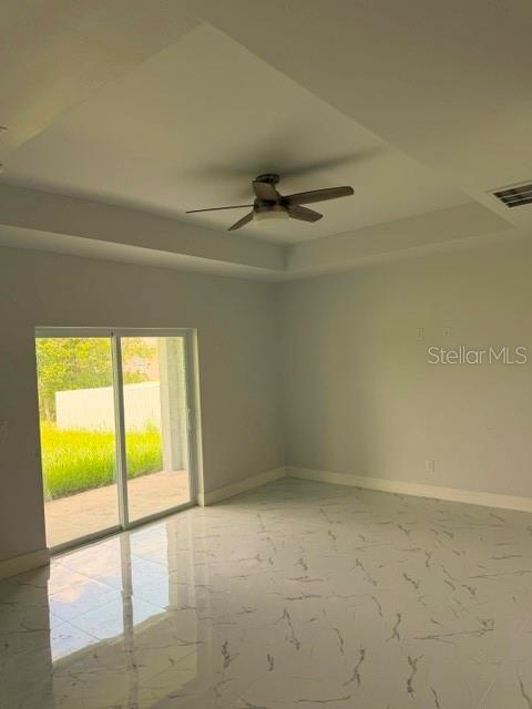 An empty room features a tray ceiling with a fan and white marble-look tile flooring — 744/746 EISENHOWER BOULEVARD, LEHIGH ACRES, FL