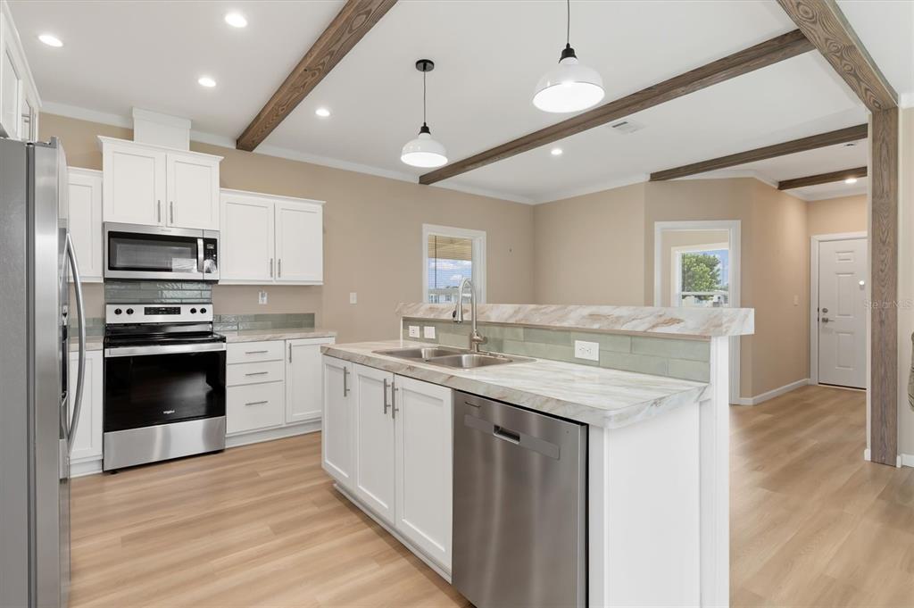 A kitchen features white cabinets, stainless steel appliances, a marble-look island, and exposed ceiling beams — 6287 GREENFINCH ROAD, ENGLEWOOD, FL