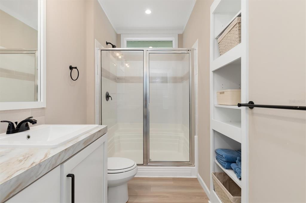 A bathroom features a vanity, a glass-enclosed shower, a toilet, and built-in wall shelving — 6287 GREENFINCH ROAD, ENGLEWOOD, FL