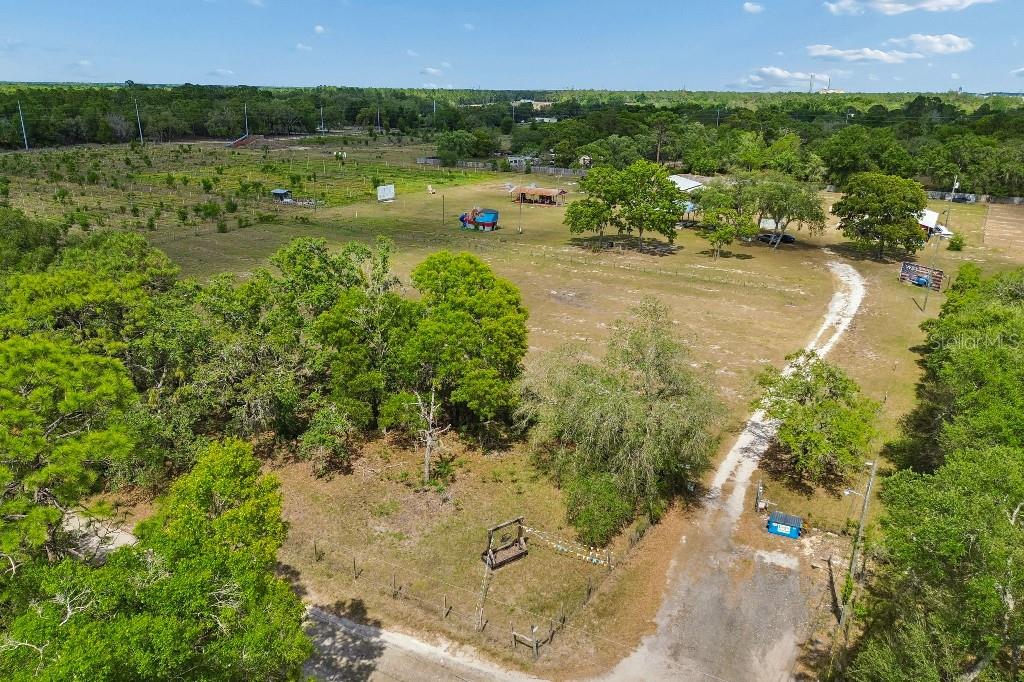 An aerial view shows a large, grassy rural property with trees, outbuildings, and a dirt driveway — 14320 FAMILY TRAIL, HUDSON, FL
