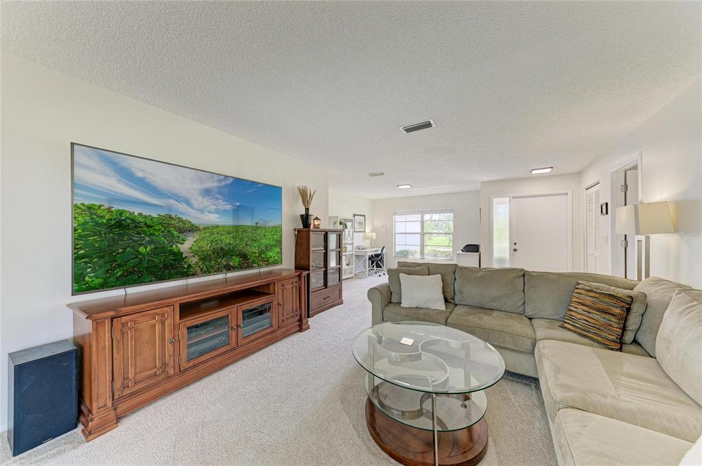 A living room features a large television, wooden media console, sectional sofa, and glass coffee table — 3980 LEMONWOOD DRIVE, SARASOTA, FL