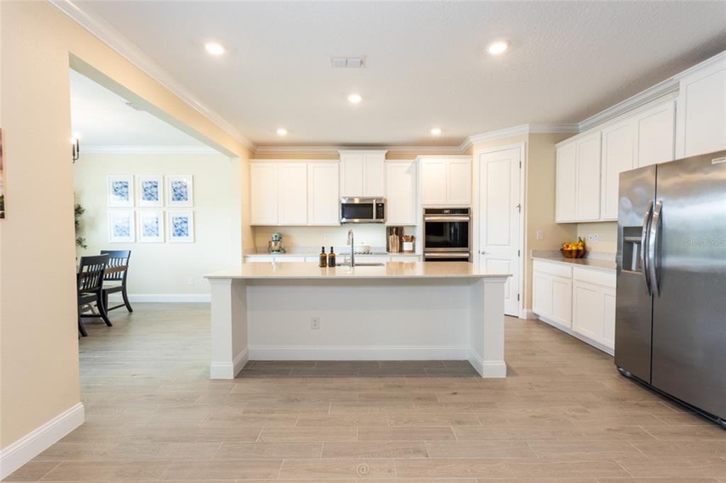 A bright kitchen features white cabinets, a central island, stainless steel appliances, and wood-look flooring — 4171 ACOMA DRIVE, ORMOND BEACH, FL