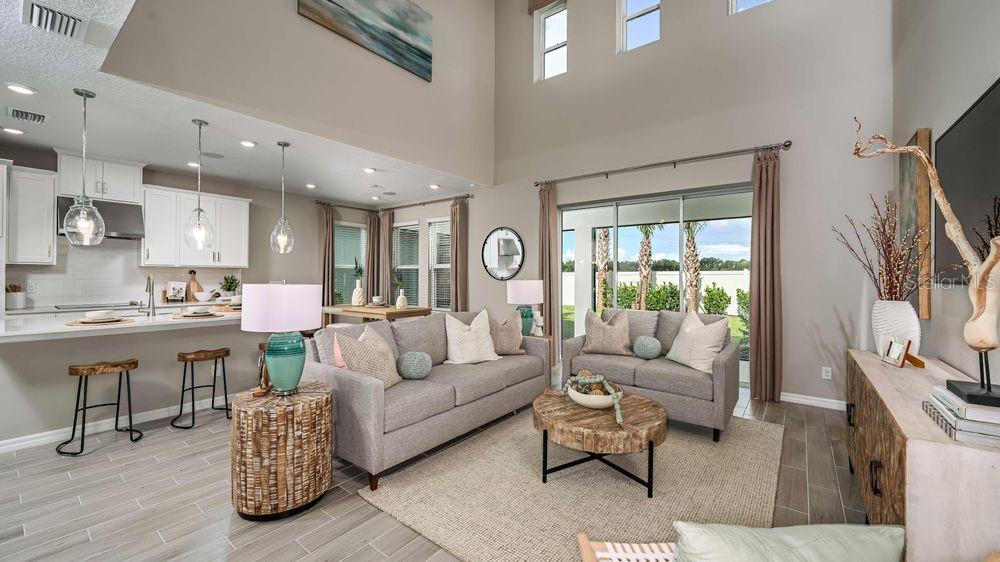 A living room with high ceilings, gray sofas, a wood coffee table, and an open kitchen — 15525 FOXTAIL LANE, NOKOMIS, FL