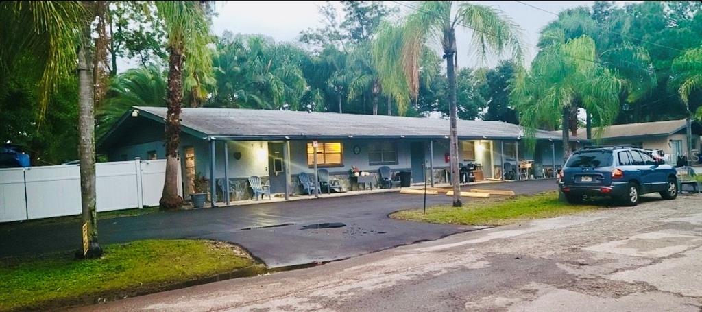 A single-story multi-unit building with a covered walkway, asphalt driveway, and surrounding palm trees — 5050 74TH STREET N UNIT 1, ST PETERSBURG, FL
