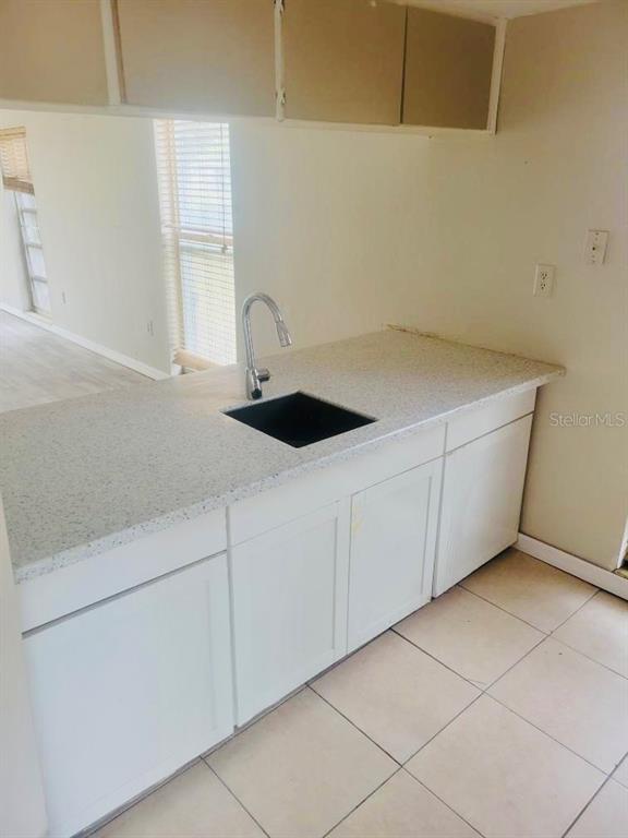 A kitchen features white cabinets, a speckled countertop, a black sink, and tile flooring — 5050 74TH STREET N UNIT 1, ST PETERSBURG, FL