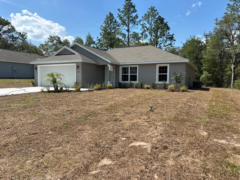 A single-story house with a beige exterior, a two-car garage, and a dry, grassy yard — 3175 W CAMILO DRIVE, DUNNELLON, FL