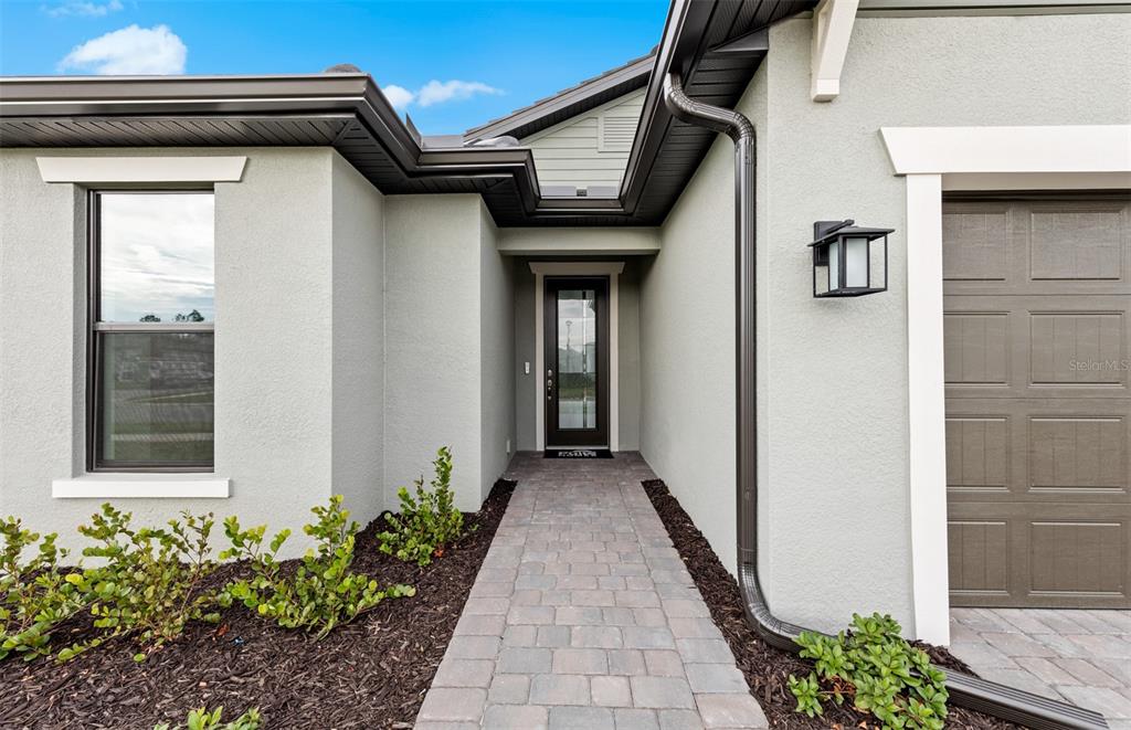 The exterior of a house features a paved walkway leading to a dark front door — 4415 LAKESIDE GROVE, NORTH PORT, FL