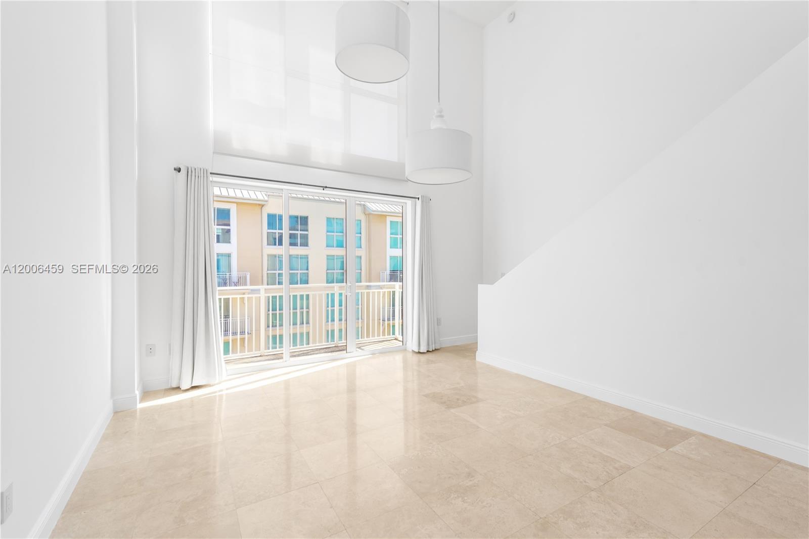 A bright, empty room features high ceilings, large pendant lights, tile floors, and balcony access — 7270 SW 88th St # B519, Miami FL 33156, MIAMI, FL