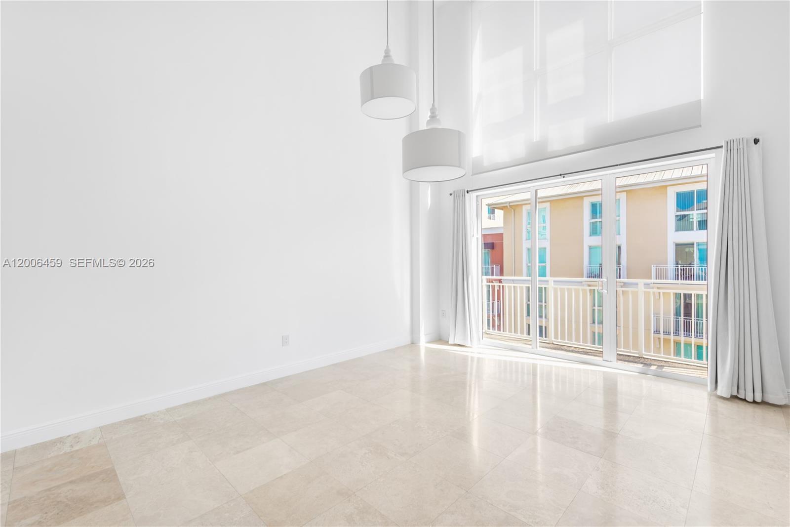 A bright, empty room features high ceilings, tile flooring, pendant lights, and a glass balcony door — 7270 SW 88th St # B519, Miami FL 33156, MIAMI, FL