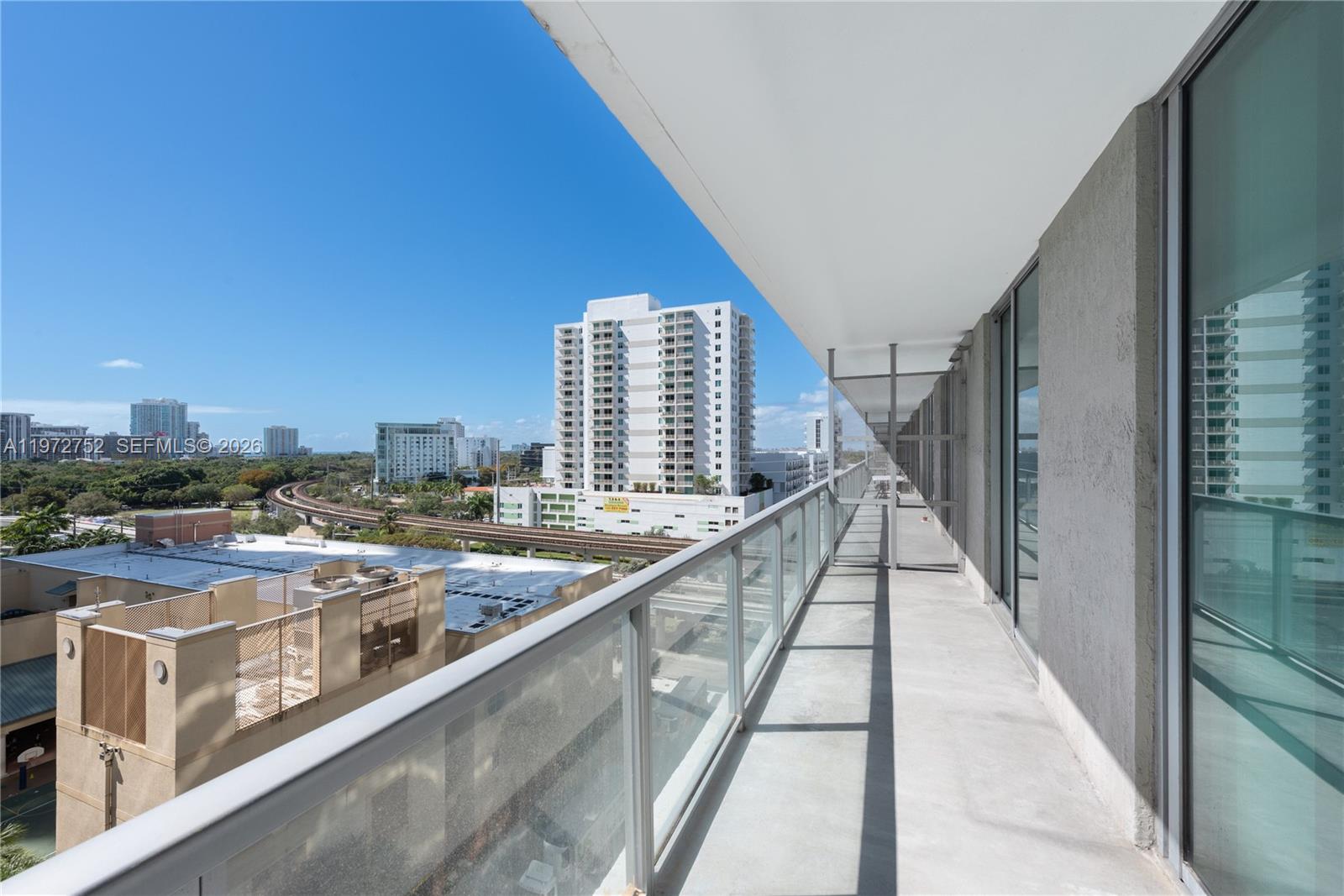 A long, narrow balcony with a glass railing overlooks a city skyline and train tracks — 79 SW 12th St, Miami FL 33130, MIAMI, FL
