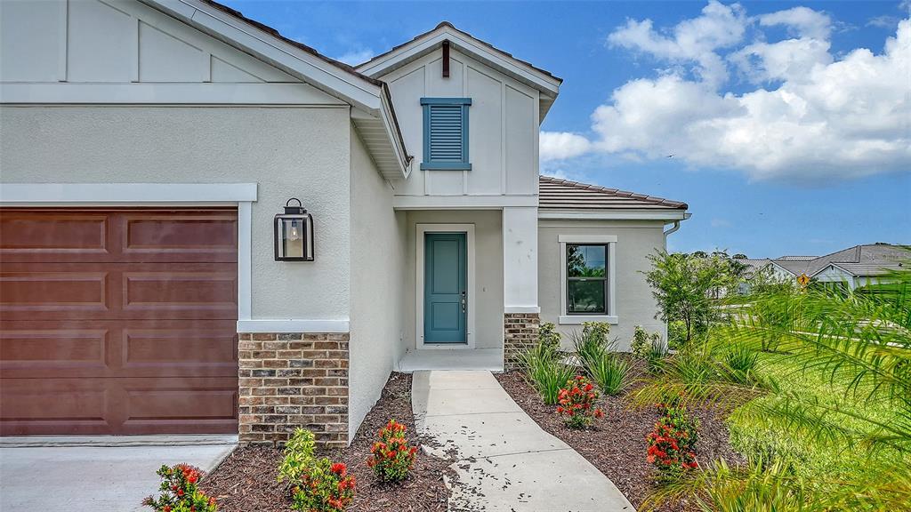A single-story house exterior features a blue front door, brown garage door, and brick accents — 6568 BIG BAYOU DRIVE, SARASOTA, FL