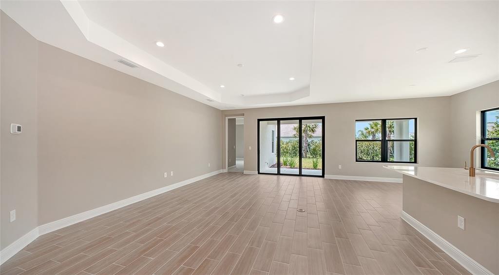 An open-concept living area with light wood-look tile flooring, recessed lighting, and sliding glass doors — 6568 BIG BAYOU DRIVE, SARASOTA, FL