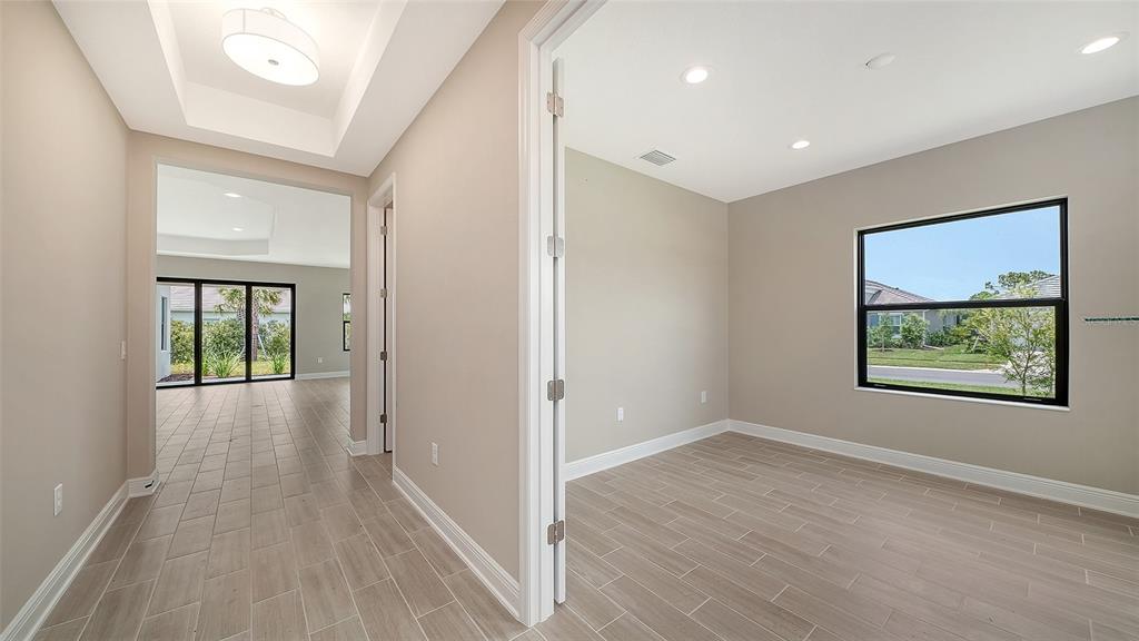 A view from a hallway into a room with light-colored tile flooring and recessed lighting — 6568 BIG BAYOU DRIVE, SARASOTA, FL