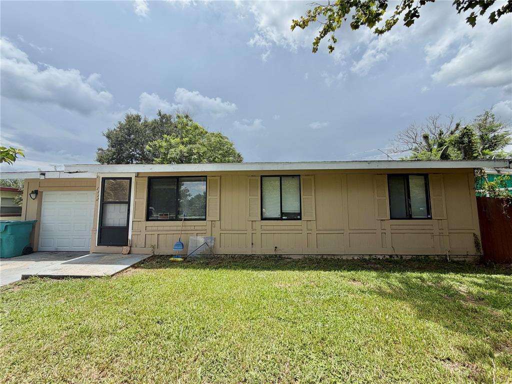 A single-story house with tan panel siding, a small garage, and a front lawn — 1312 LAWNE BOULEVARD, ORLANDO, FL