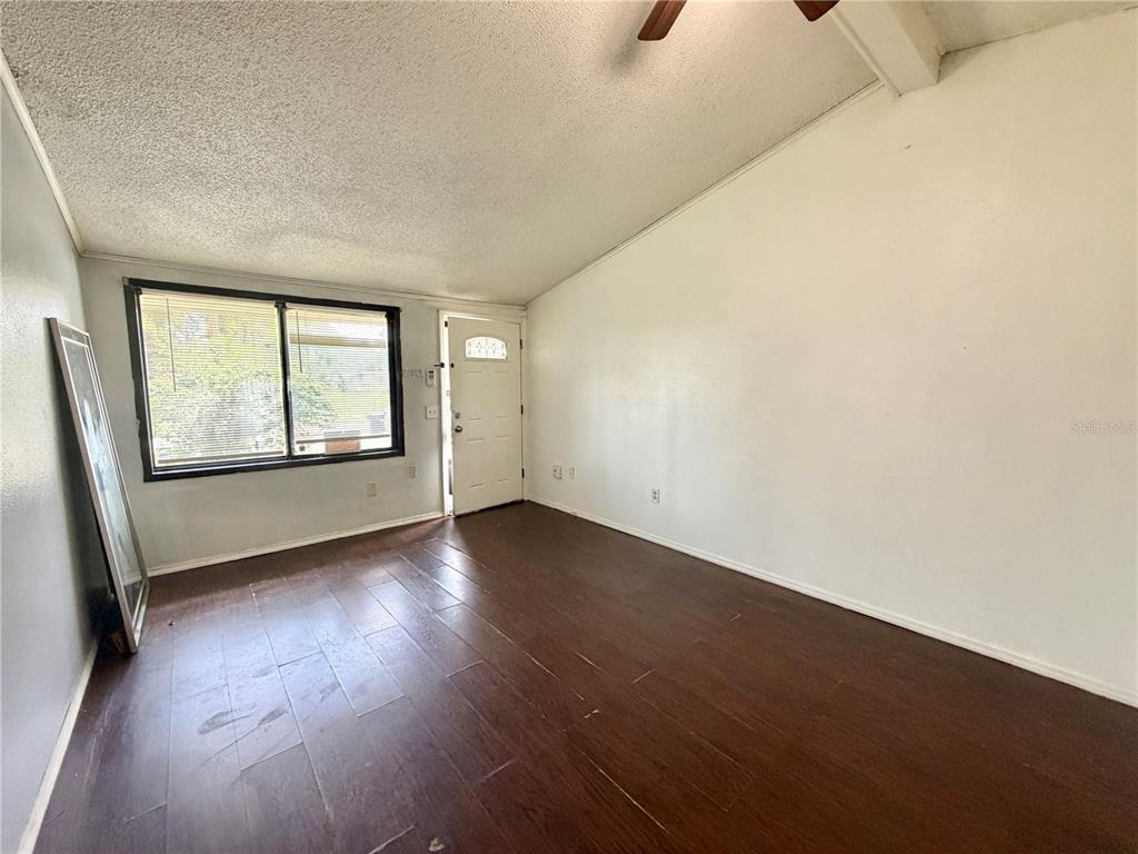 An empty room features dark wood-look flooring, white walls, a vaulted ceiling, and a window — 1312 LAWNE BOULEVARD, ORLANDO, FL