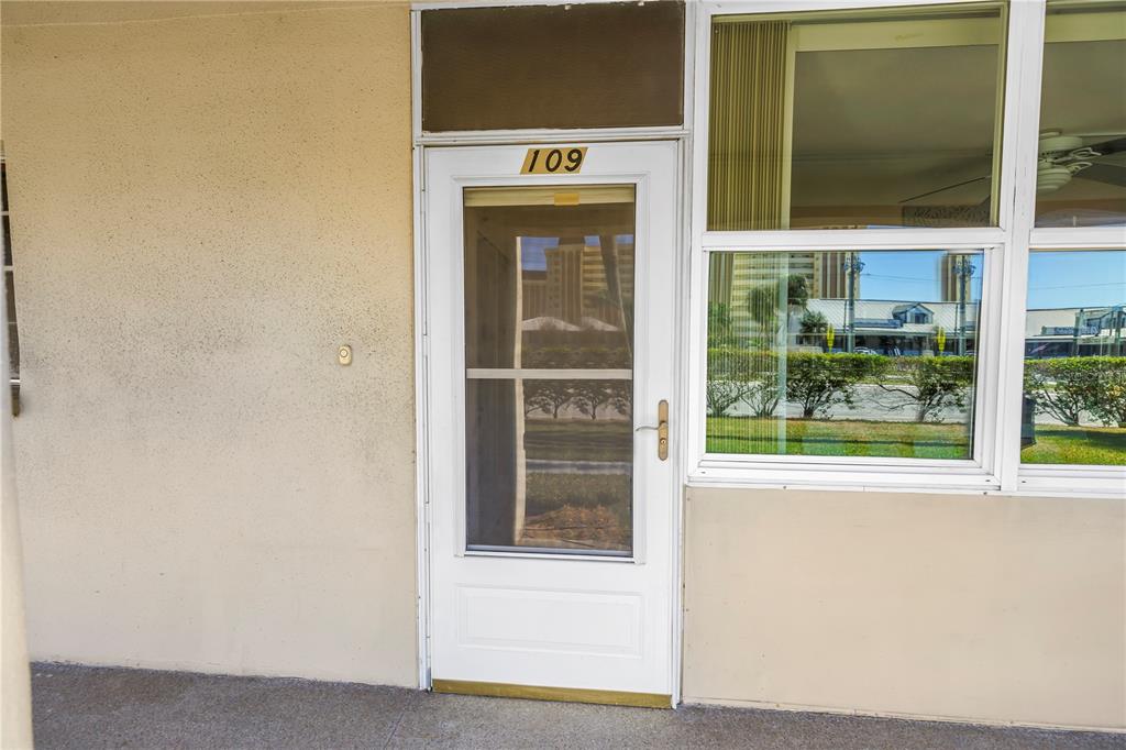 A white exterior door labeled 109 sits beside a large window on a concrete walkway — 4455 DUHME ROAD UNIT 109, ST PETERSBURG, FL