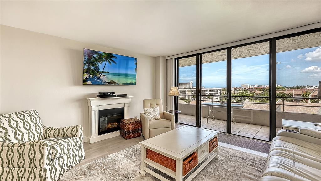 A living room features a fireplace, a television, a patterned armchair, and a balcony view — 6415 MIDNIGHT PASS ROAD UNIT 602, SARASOTA, FL