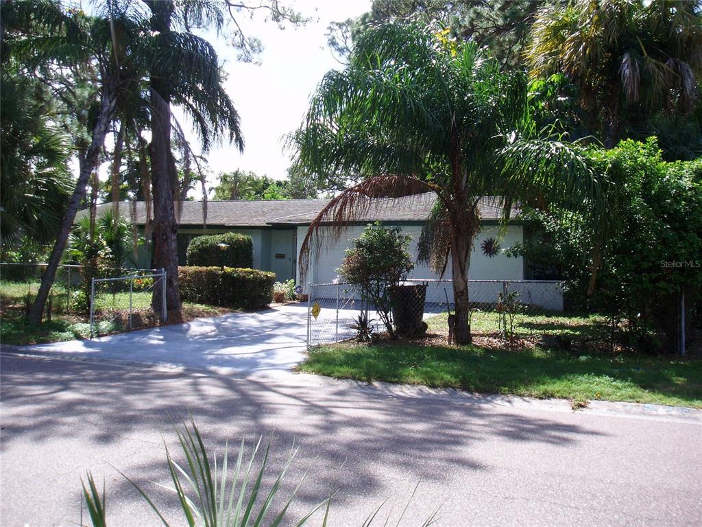 A single-story house with a concrete driveway, chain-link fence, and palm trees in front — 120 SW MONROE CIRCLE N, ST PETERSBURG, FL