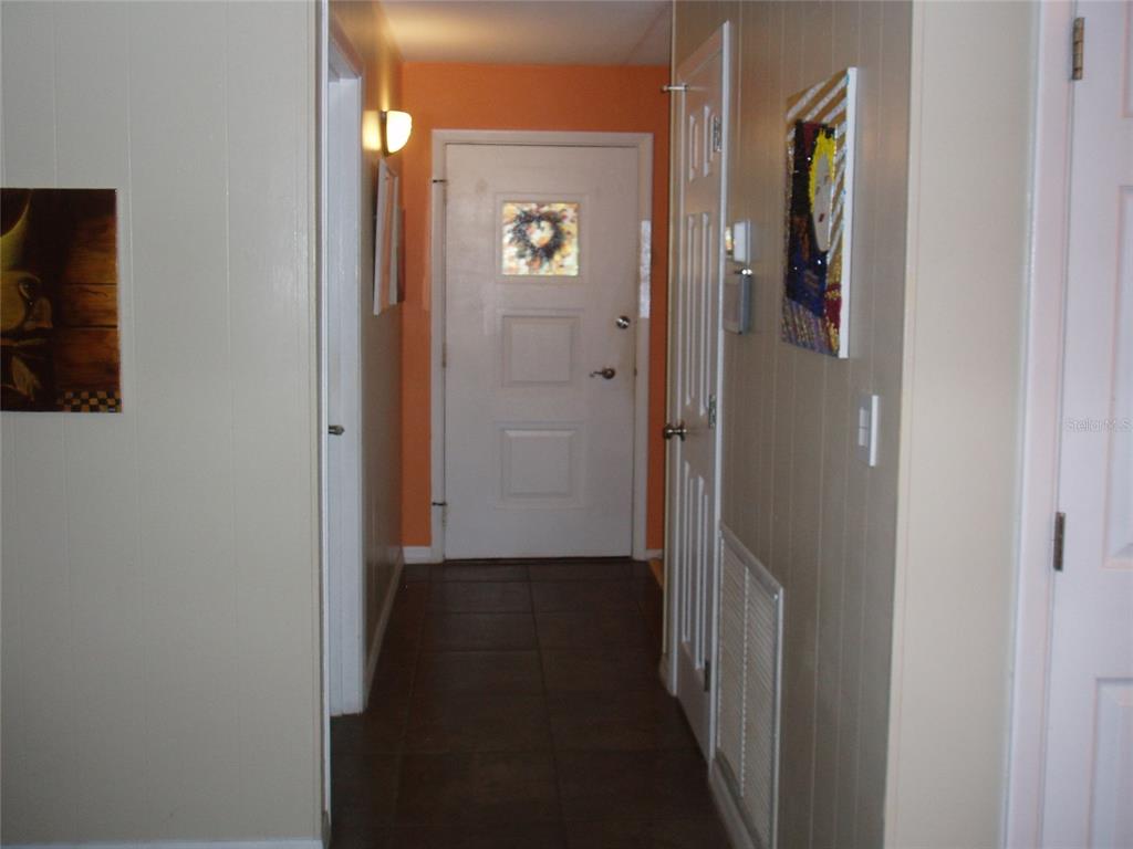 A hallway with tiled flooring leads to a white front door with a decorative window — 120 SW MONROE CIRCLE N, ST PETERSBURG, FL
