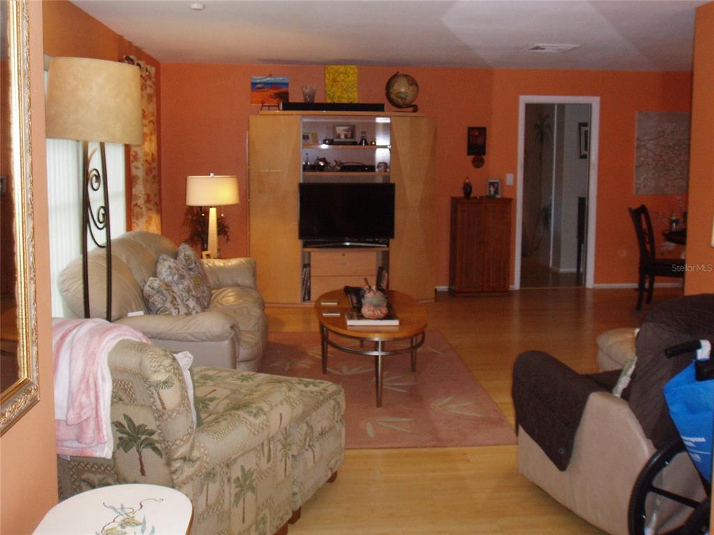 A living room features orange walls, light wood flooring, an entertainment center, and beige furniture — 120 SW MONROE CIRCLE N, ST PETERSBURG, FL