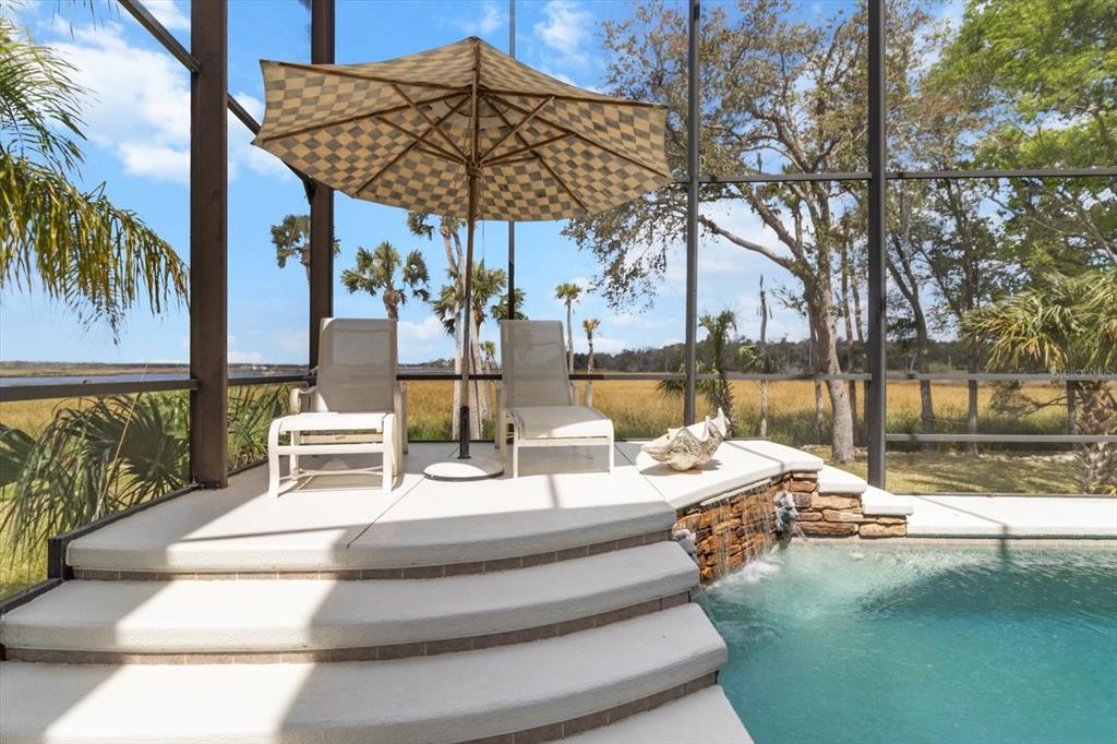 A screened-in pool deck features two lounge chairs, a checkered umbrella, and a stone waterfall — 11927 W TIMBERLANE DRIVE, HOMOSASSA, FL